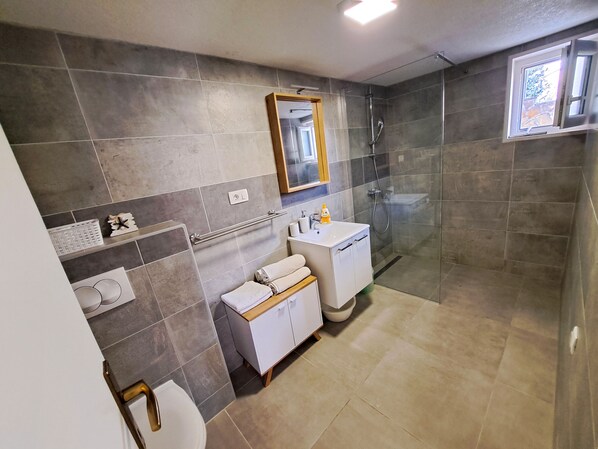 A modern bathroom with a glass shower enclosure, a white sink, and a vanity with a mirror. - Apartments Ivanka (Supetar)