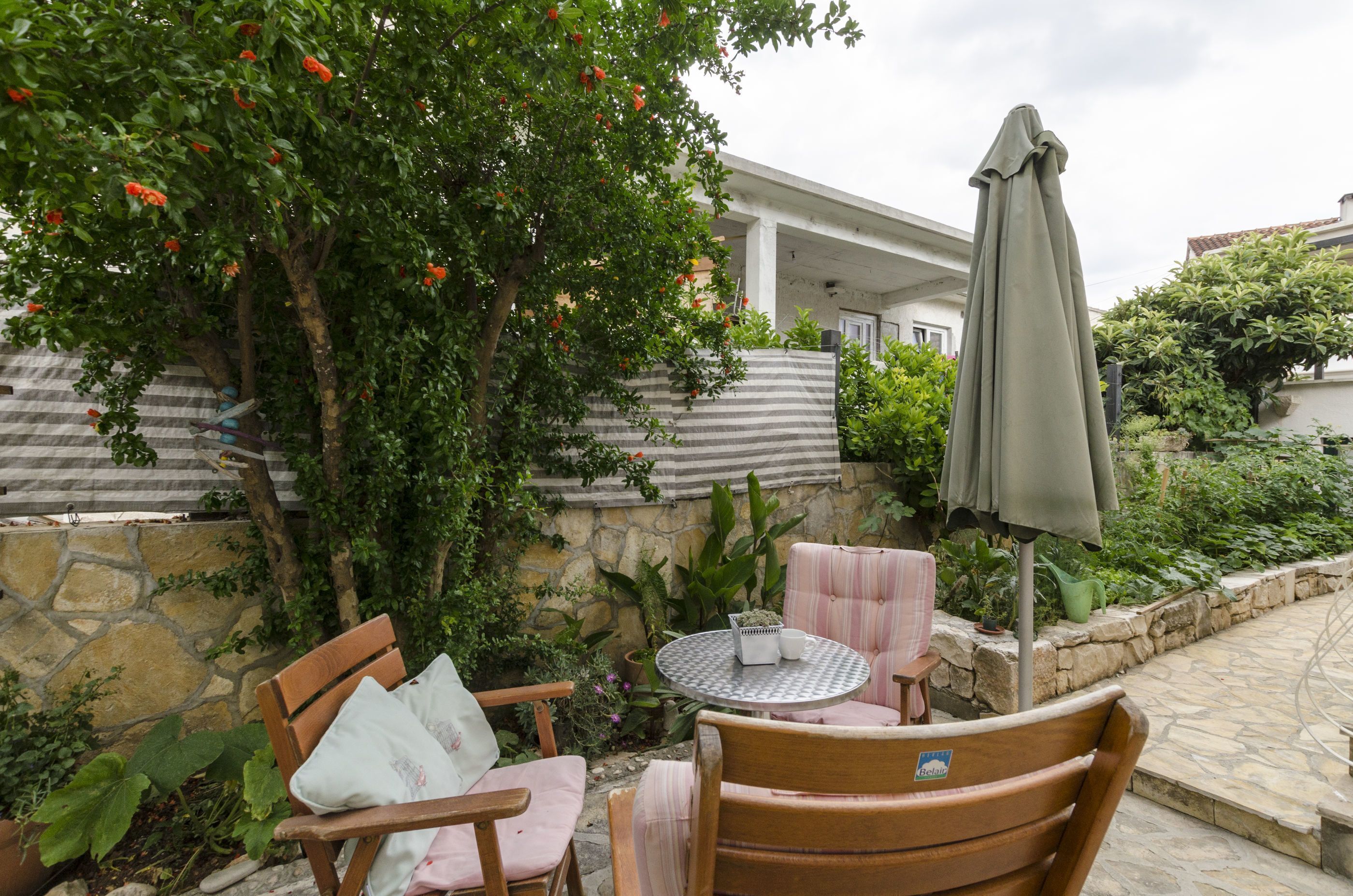 An outdoor patio area with stone walls, a wooden table, two chairs, and a green umbrella.