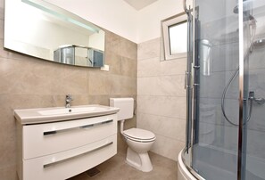 A modern bathroom with a white sink, toilet, and glass-enclosed shower. - Apartment Dora (Duce)