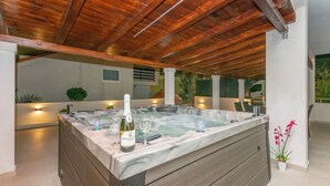 Un jacuzzi con una botella de vino y copas, vigas de madera en el techo y una planta en maceta.