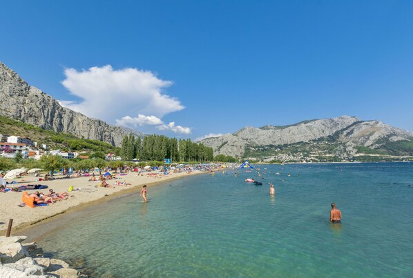 A beach with clear water, people swimming and sunbathing, and mountains in the background. - Apartment Dora (Duce)
