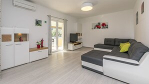 Una sala de estar moderna con un sofá gris, un televisor sobre un mueble de madera y un armario blanco decorado con objetos.