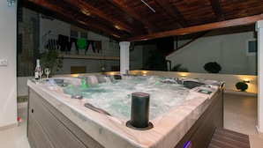 Un jacuzzi con techo de madera y paredes de piedra, rodeado por un balcón con plantas.