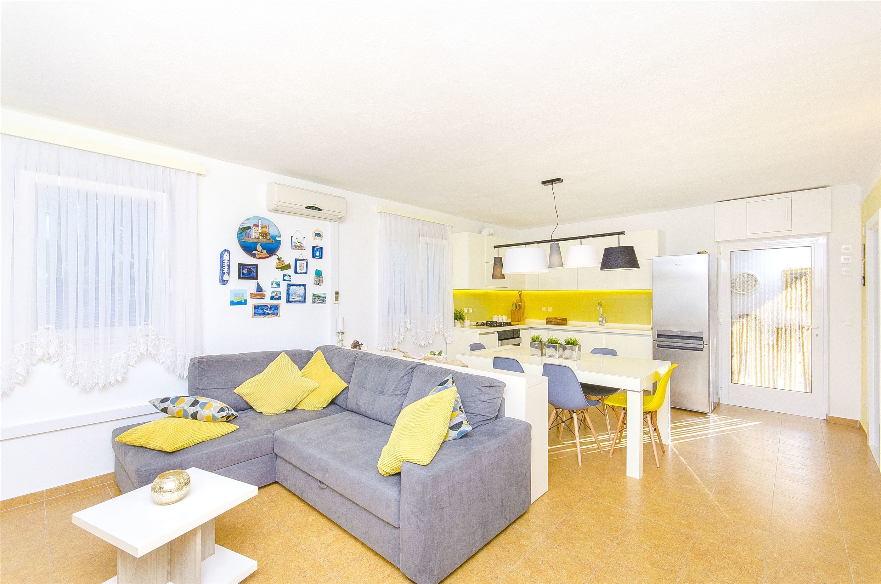 A modern living room with a grey sofa, yellow cushions, a white coffee table, and a dining area with a yellow chair.