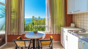 A balcony with a table and chairs, a view of the sea, and a kitchen area with cabinets and a stove. - Apartments Kunac (Podgora)
