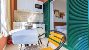 A compact kitchen with white cabinets, a microwave, and a sink. There's a small dining table with a bowl on it and a chair. - Apartments Kunac (Podgora)