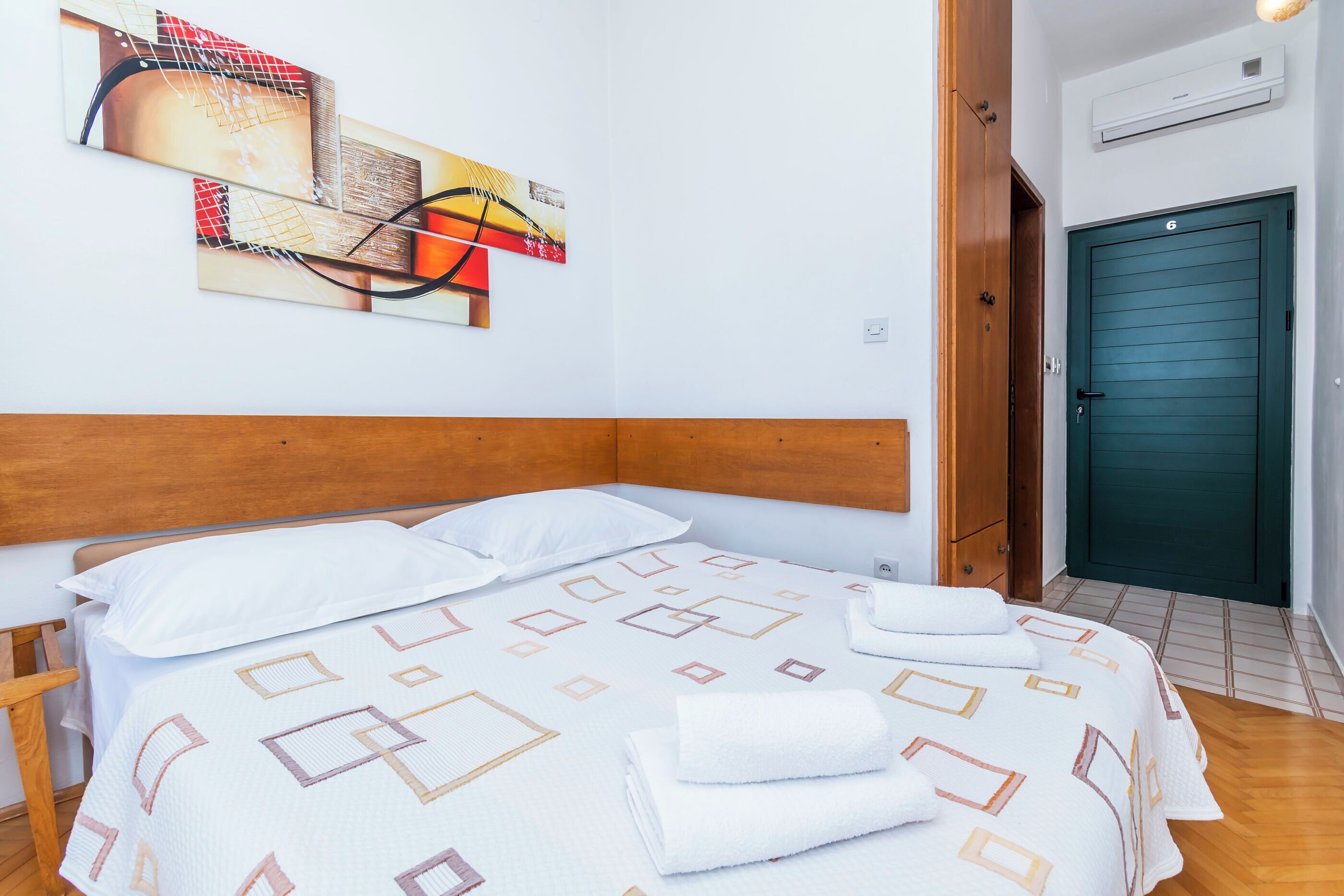 A neatly made bed with a patterned bedspread, a wooden headboard, and a wall-mounted abstract painting.