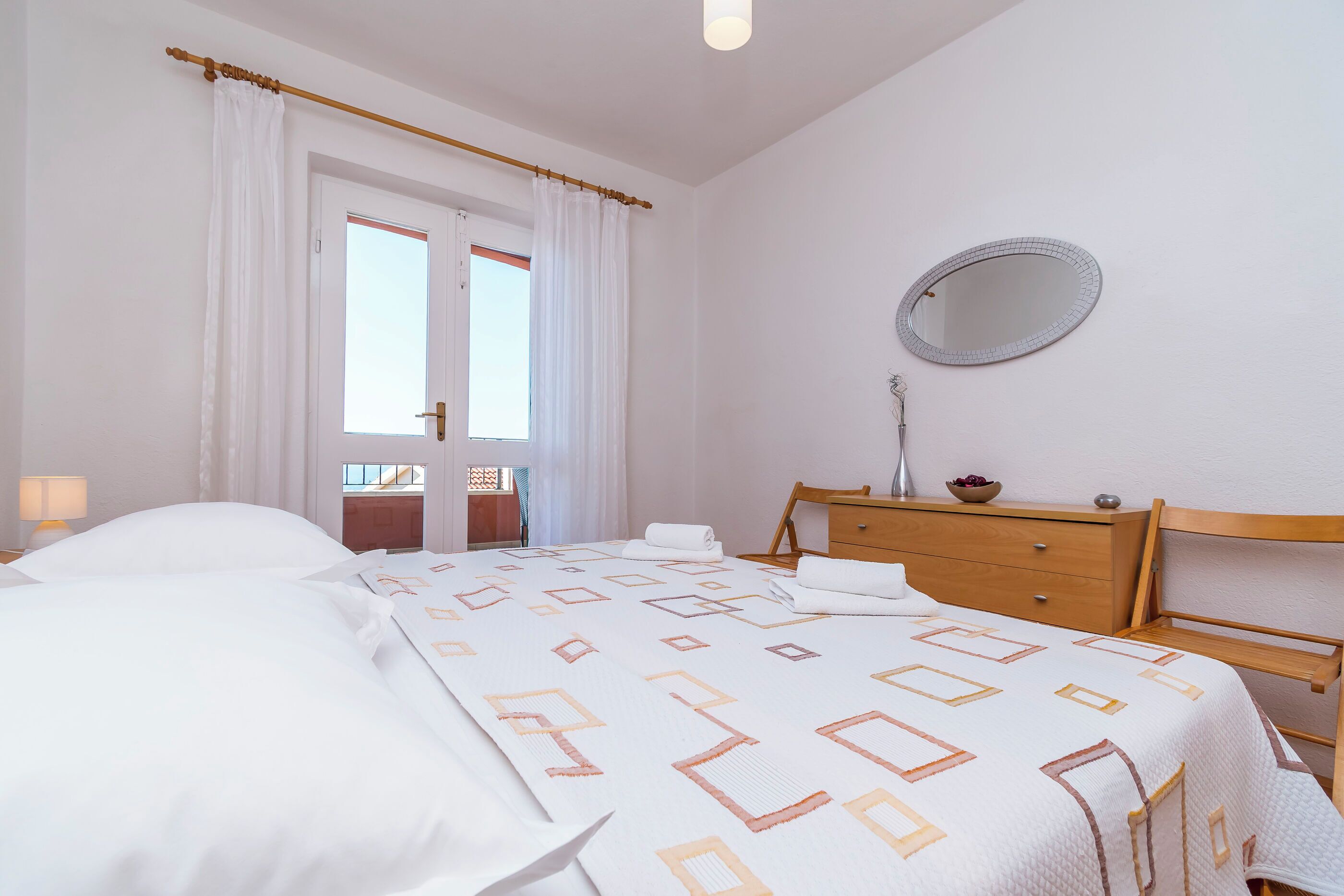 Quarto com cama, cómoda de madeira, espelho e janela com cortinas.