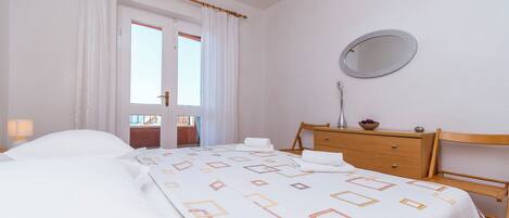 Quarto com cama, cómoda de madeira, espelho e janela com cortinas.