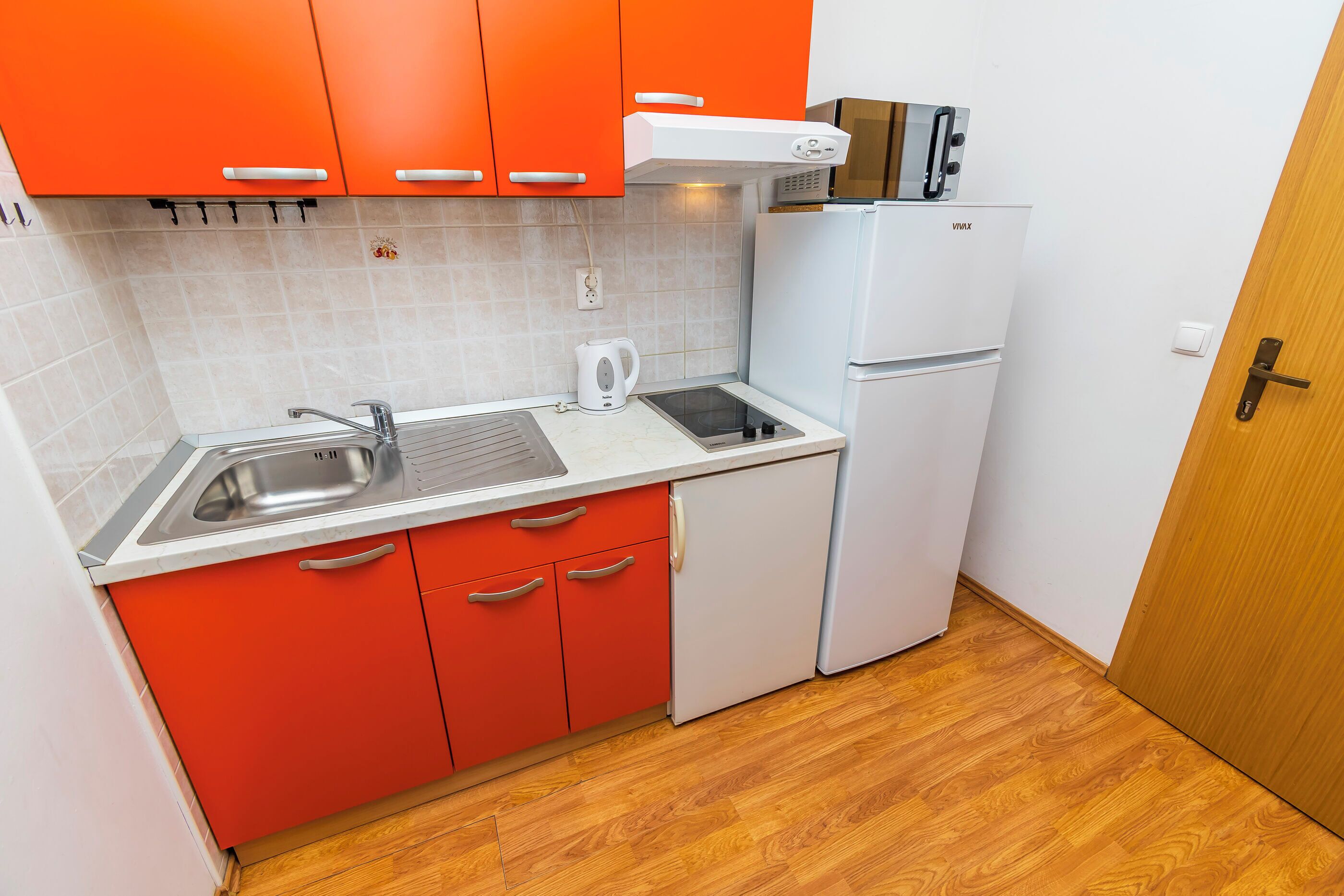 A compact kitchen with red cabinets, a white countertop, a sink, a microwave, and a refrigerator.