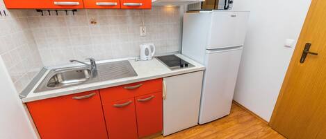 A compact kitchen with red cabinets, a white countertop, a sink, a microwave, and a refrigerator.