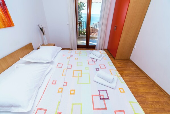 Habitación de hotel con cama, suelo de madera, vista al mar a través de una puerta corrediza y una puerta roja.