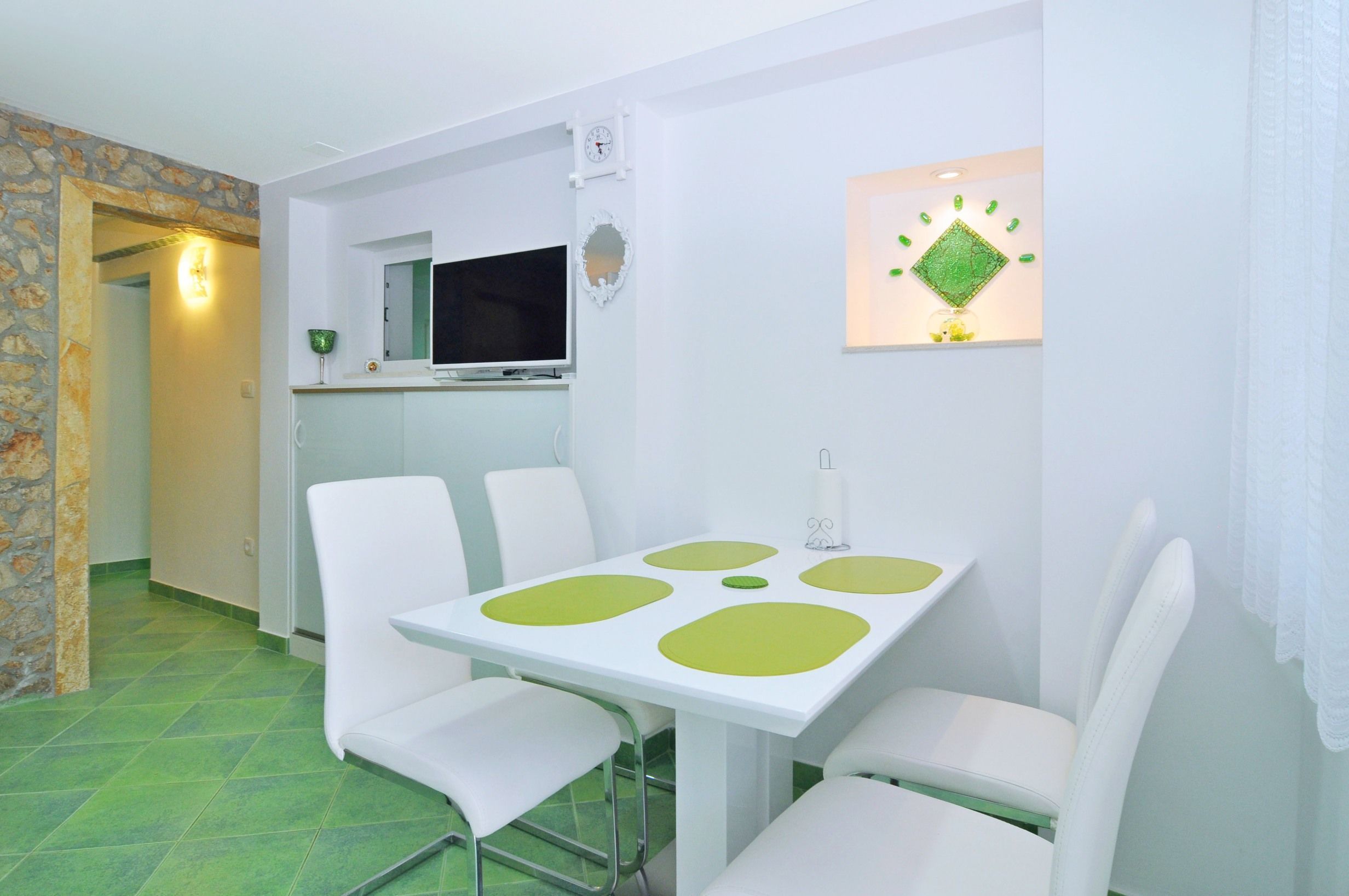 A dining area with a white table and chairs, a television, and a clock on the wall.