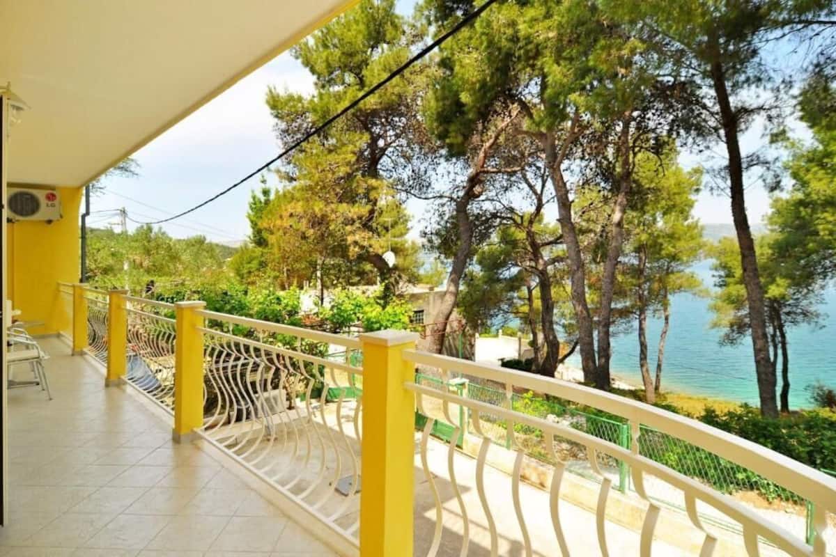 A balcony with a yellow railing overlooking a coastal area with trees and a view of the sea.