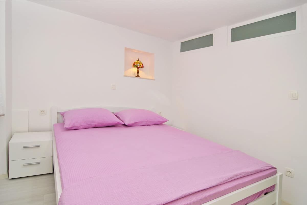 A bedroom with a bed, a nightstand, a lamp, and a small window.
