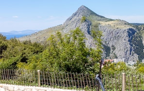 A mountainous landscape with a prominent peak, a fence in the foreground, and a distant cityscape. - House Marta (Omis)