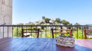 Ein Holztisch mit einem Steintopf auf einem Balkon mit Blick auf einen Hügel und Grünflächen.