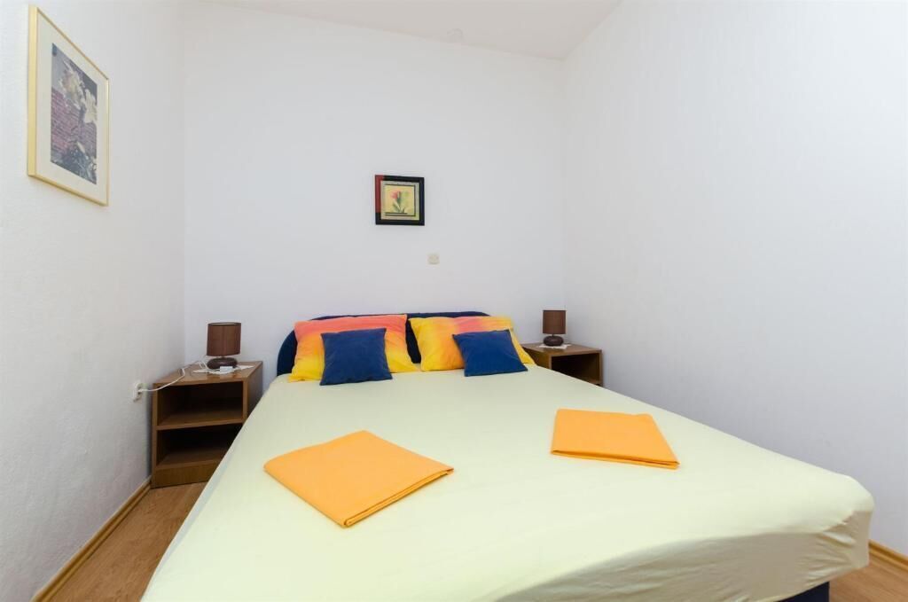 A single bed with a light-colored mattress, two bedside tables with lamps, and a framed picture on the wall.