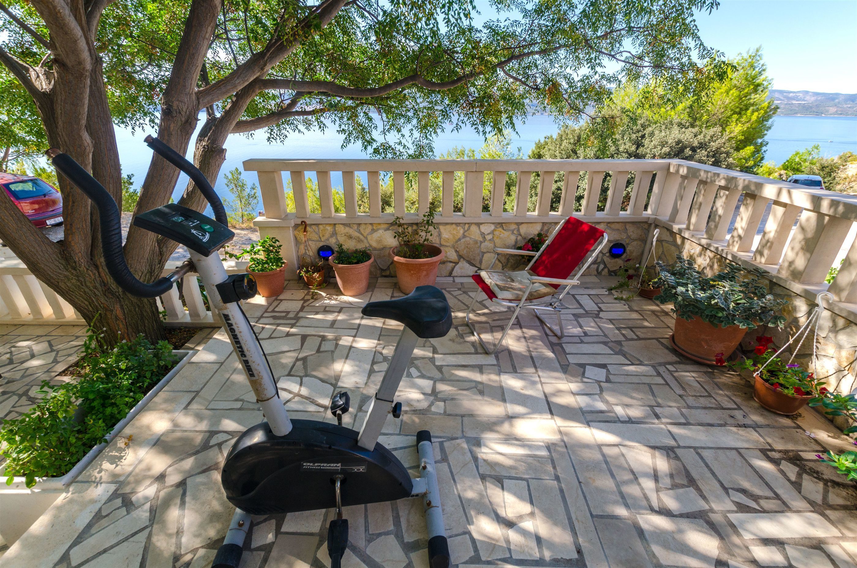 An outdoor exercise area with an elliptical machine, potted plants, and a red chair.