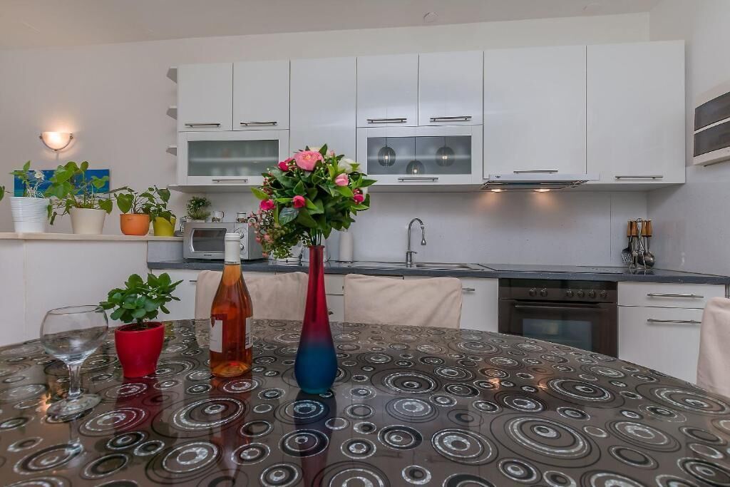 A modern kitchen with white cabinets, a microwave, and a stove. There is a table with a patterned tablecloth and two vases with flowers.