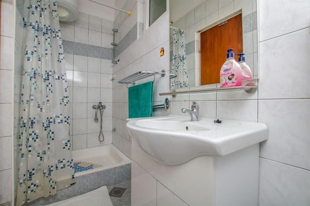 A bathroom with a white sink, a shower with a patterned curtain, and a shelf with toiletry bottles.
