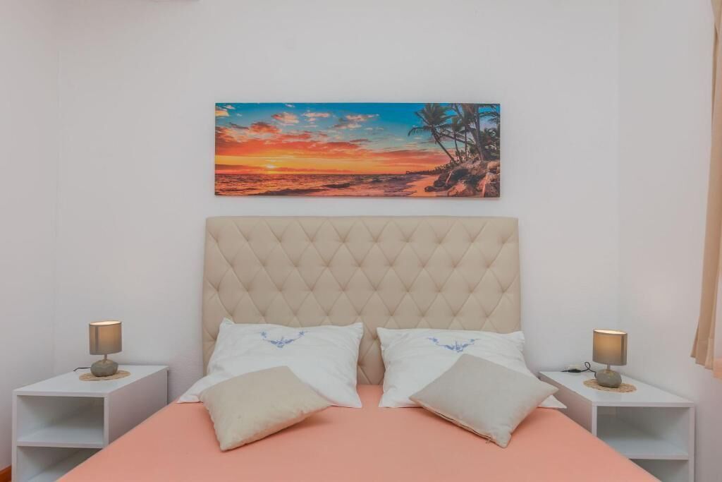 Un dormitorio con una cama grande, dos mesitas de noche y una pintura de una puesta de sol sobre una playa.