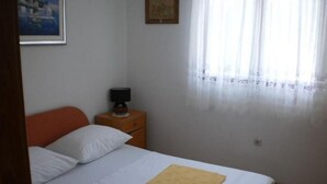 A bedroom with a bed, a nightstand, a lamp, and a window with sheer curtains. - Apartment Tomislav (Okrug Gornji)