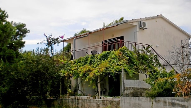 Ein einstöckiges Gebäude mit Balkon, umgeben von Grün.