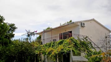 Edificio de un piso con balcón, rodeado de vegetación.