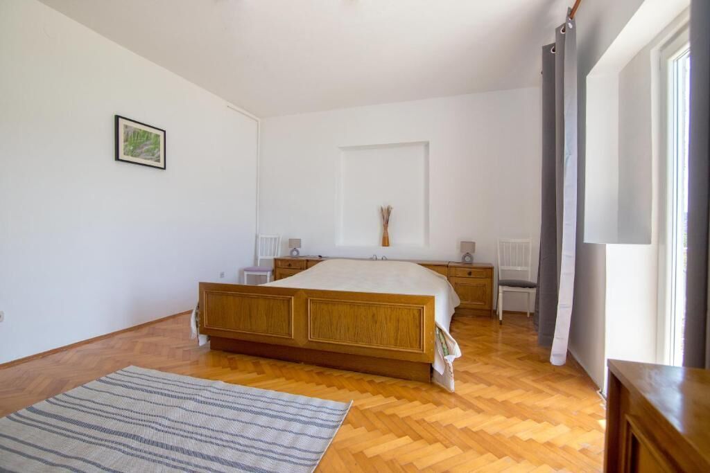 Un dormitori amb un llit de fusta, una taula de nit, una finestra amb cortines i un quadre al mur.