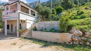A two-story house with a balcony, a concrete retaining wall, and a mountainous backdrop. - Apartment Josipa (Omis)