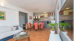A modern living room with a glass coffee table, a sofa, and a dining area with red chairs. - Apartment Josipa (Omis)