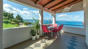 A balcony with a table and chairs, potted plants, and a view of the sea. - Apartment Josipa (Omis)