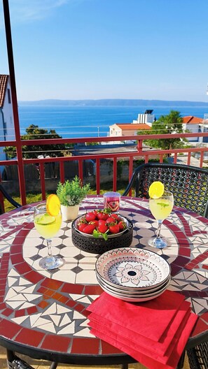 A table with a patterned tablecloth, a bowl of strawberries, a glass of yellow drink, and a plate with a decorative design. - Apartment Anita (Okrug)