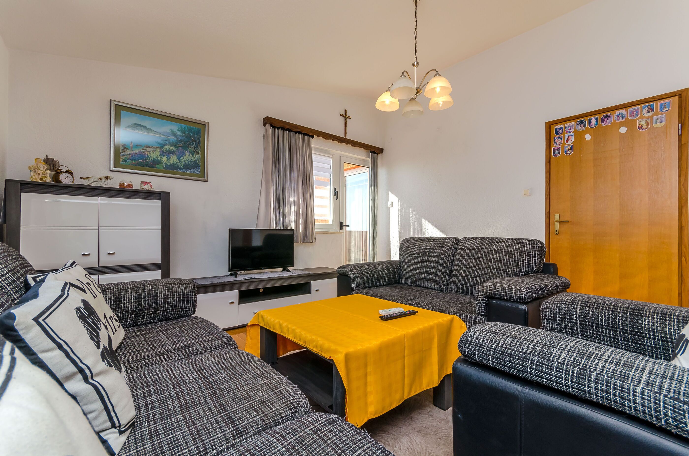 Una sala de estar con un sofá, una mesa amarilla, un televisor y una puerta de madera decorada.