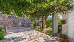 A stone courtyard with a tiled floor, potted plants, and a pergola with grapevines. - Apartment Dorijana (Porec)