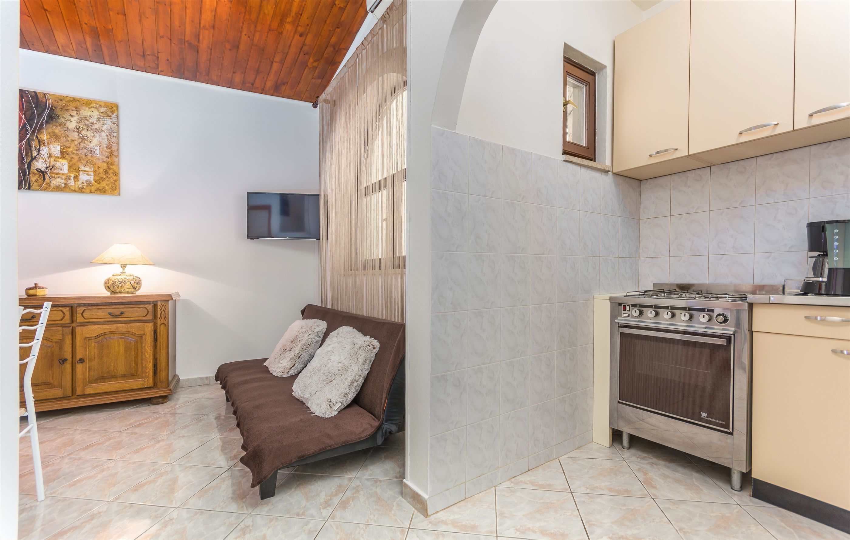 Una cucina compatta con un fornello, un pensile in legno e un divano con cuscini.