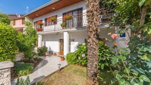 A two-story building with a balcony adorned with potted plants and flowers. - Apartment Dorijana (Porec)