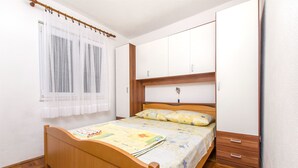 A bedroom with a wooden bed, a white wardrobe, and a window with sheer curtains. - Apartment Vojka (Vrbanj)