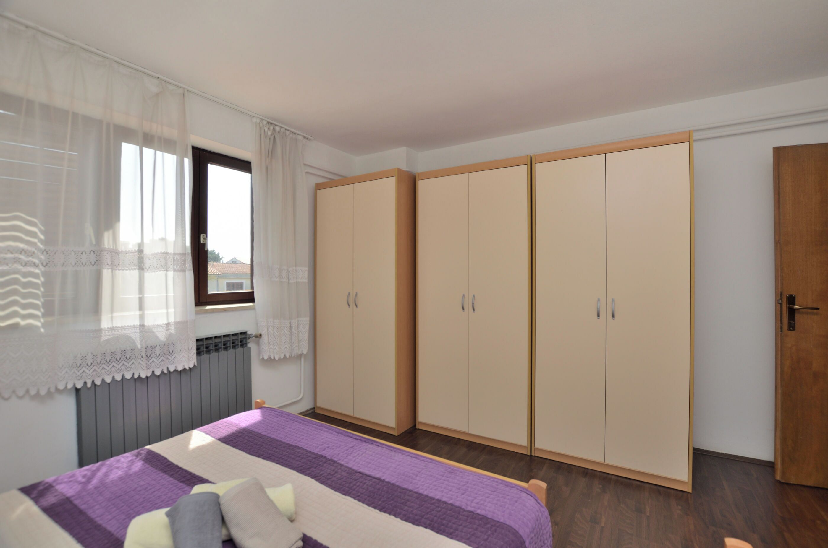 Une chambre à coucher avec un lit, une fenêtre avec des rideaux légers et une armoire à deux portes.