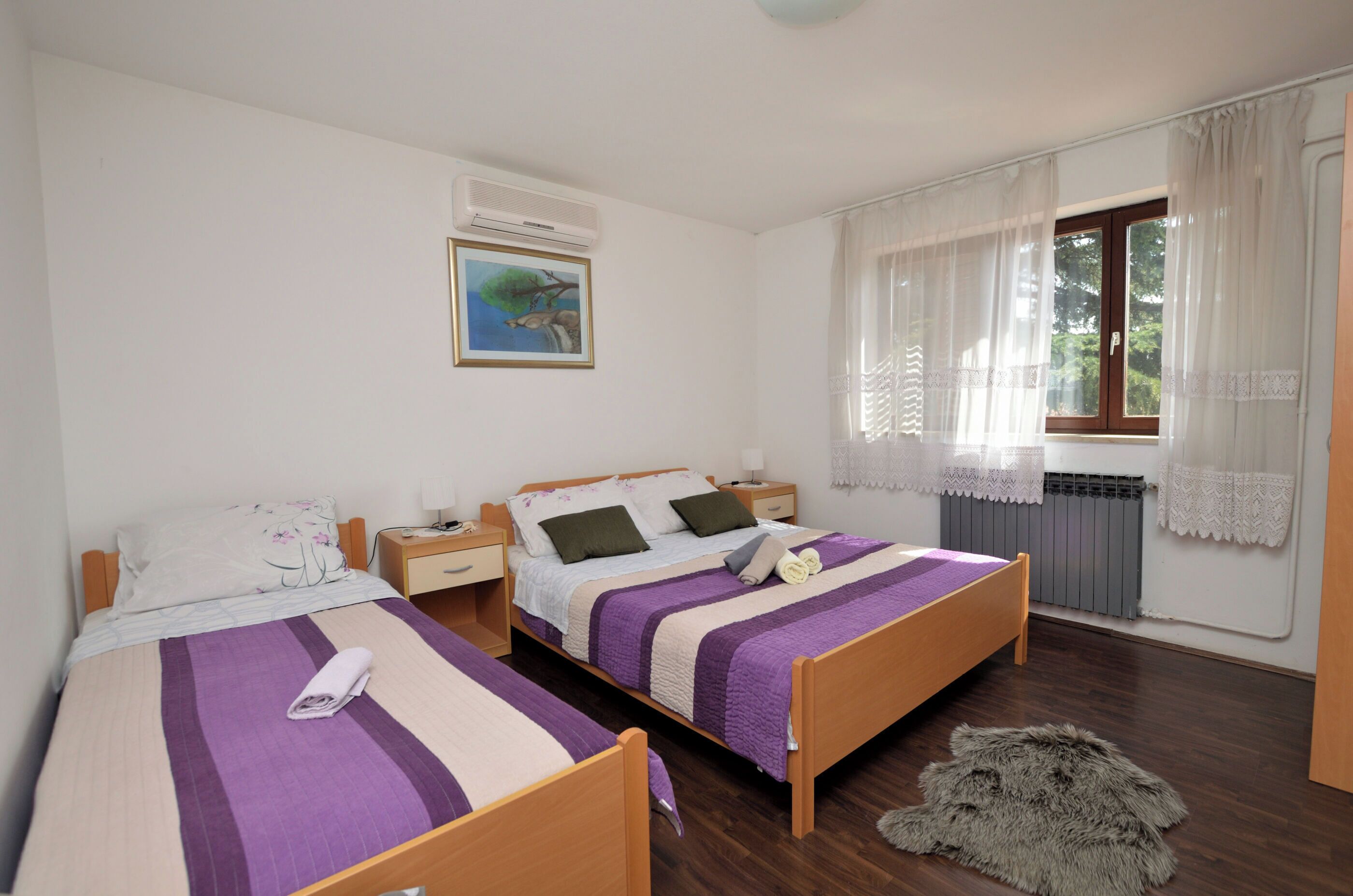 Un dormitorio con dos camas, una ventana con cortinas, un radiador y un cuadro en la pared.