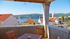 A balcony with a wooden table and chairs, overlooking a coastal town with buildings and a church. - Apartment Mario (Sumartin)