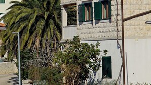 A white building with green shutters, a stone wall, and a palm tree. - Apartment Mario (Sumartin)