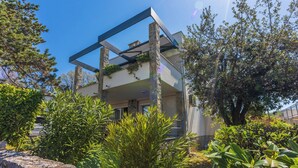 A modern two-story house with a balcony, surrounded by lush greenery and trees. - Apartment Vito (Njivice)