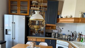 A kitchen with a wooden table, two chairs, a refrigerator, an oven, and a hanging light fixture. - Apartment Vito (Njivice)