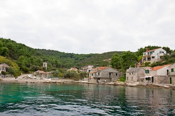 A coastal village with stone buildings, a clear view of the sea, and a hilly backdrop.