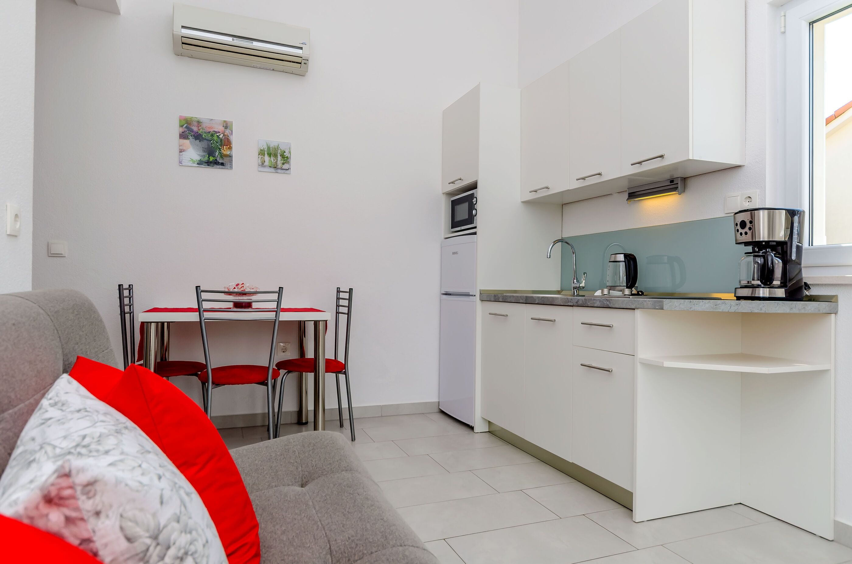 A compact kitchen with white cabinets, a microwave, and a coffee maker. There is a dining area with a table and chairs.
