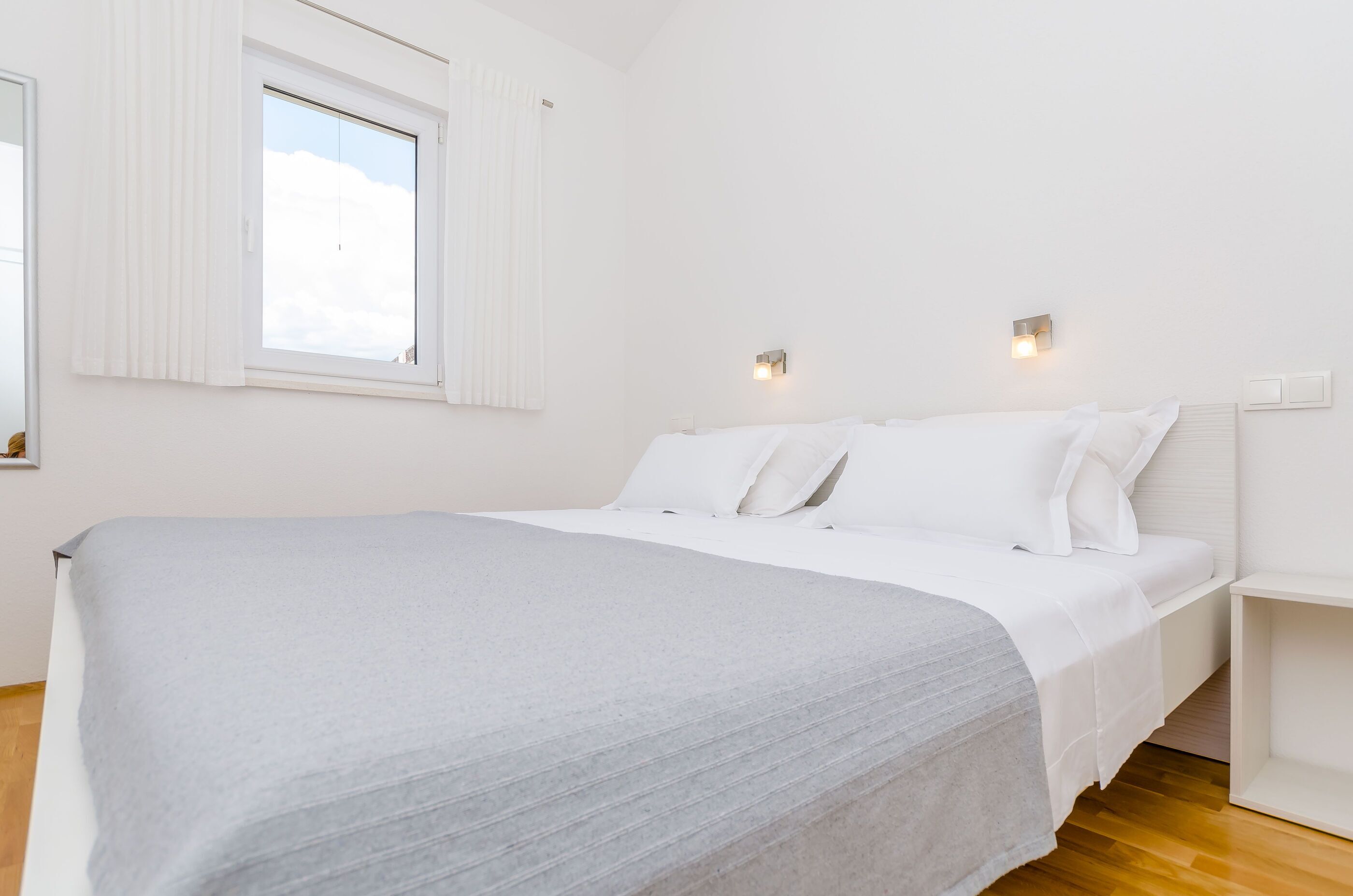 A minimalist bedroom with a large bed, white bedding, and a window with blinds.