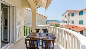 Ein Balkon mit Tisch und Stühlen, einer Schiebeglastür und Blick auf das Meer und Gebäude.