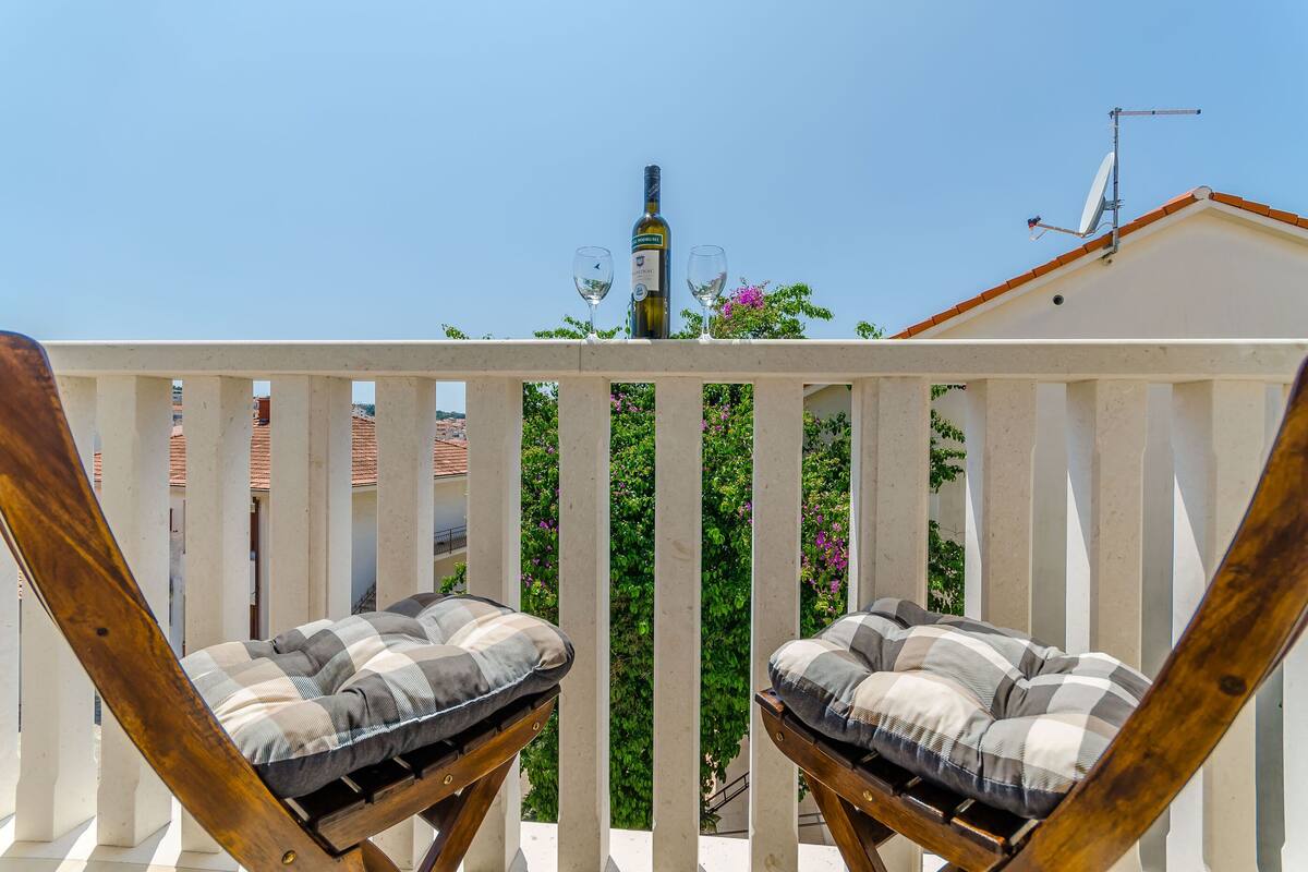 A balcony with two wooden chairs and a bottle of wine on a railing.